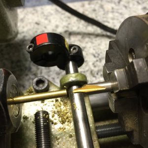 A brass rod turned in a collet an a center drill starting a hinge rod hole.